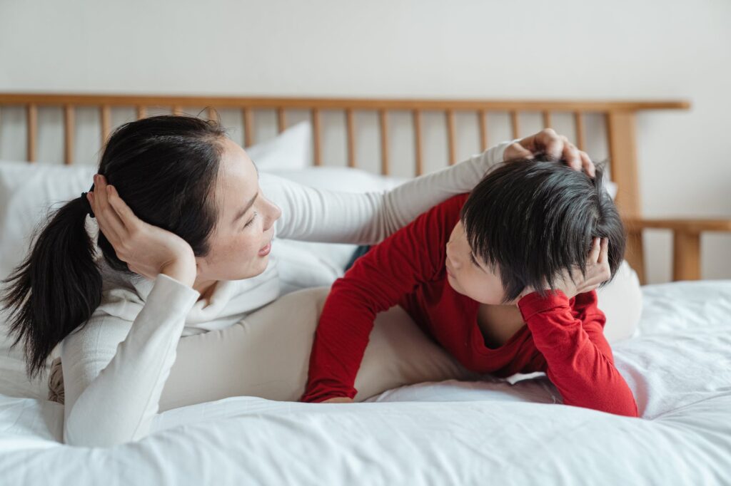 caring mother patting little son on head on bed