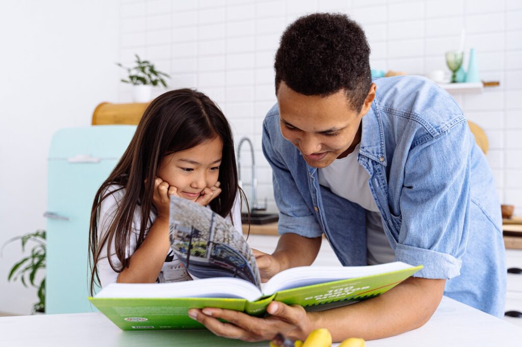 photograph of a child reading a book with her father